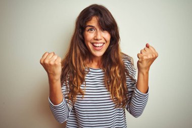 Beyaz tenli arka plan üzerine çizgili tişört giyen genç ve güzel bir kadın kollarını kaldırarak ve açık gözlerle başarıyı kutluyor. Kazanan konsept.