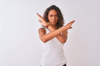 Genç Brezilyalı bir kadın, günlük tişört giyip izole edilmiş beyaz arka planda duruyor. Reddedilmiş yüz ifadesi, kollarını kavuşturarak negatif işaret veriyor, kızgın yüz ifadesi takınıyor.