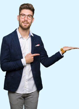 Hayret ve el ile sunulması ve parmak ile işaret ederken kameraya gülümseyen gözlüklü genç yakışıklı iş adamı.