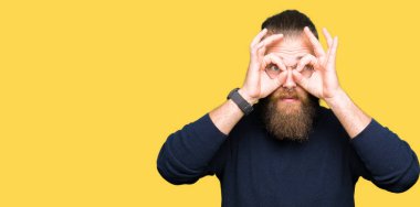 Gözlük ve dilini, parmaklarının arasından baktığını yapışmasını dürbün gibi ok jest yapıyor boğazlı kazak giyen genç sarışın adam. Deli ifade.