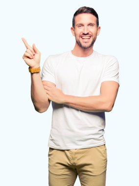 Yakışıklı adam, yüzünde kocaman bir gülümseme ile rahat beyaz t-shirt giyen kameraya bakarak yan el ve parmak ile işaret.