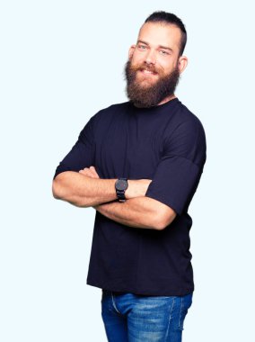 Rahat t-shirt mutlu yüz ile gülümseyen giyen genç sarışın adam kameraya seyir silah geçti. Olumlu bir kişi.