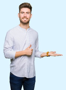 Genç yakışıklı gösteren palm el ve yukarıya, mutlu ve neşeli gülümseyen baş parmakları Tamam jest yapıyor adam