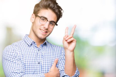 Mutlu yüz zafer işareti yaparken kameraya göz kırpıyor ile gülümseyen izole arka plan üzerinde gözlük takan yakışıklı delikanlı. İki numaralı.