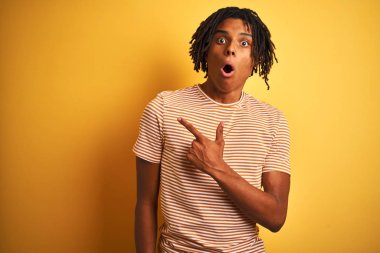 Sarı arka plan üzerinde duran çizgili t-shirt giyen Afro bir adam. Parmakla yüzünü göstererek şaşırmış ve ağzı açık kalmış..