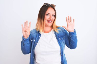 İzole edilmiş beyaz arka plan üzerinde duran kot gömlek giyen güzel bir kadın dokuz numaralı parmaklarıyla işaret ederken kendinden emin ve mutlu bir şekilde gülümsüyor..