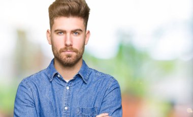 Yüz çapraz silah ile rahat kot gömlek şüpheci ve sinir, onaylamayan ifade giyen genç yakışıklı sarışın adam. Negatif kişi.