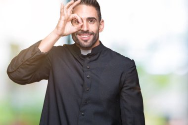 Genç Hıristiyan rahip gülümseyen, parmakları ile mutlu yüz üzerinden seyir göz el ile ok jest yapıyor izole arka plan üzerinde.