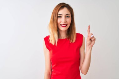 Kırmızılı iş kadını zarif kırmızı elbiseler giyiyor. İzole edilmiş beyaz arka planda duruyor. Bir numarayı işaret ediyor ve gülümsüyor..