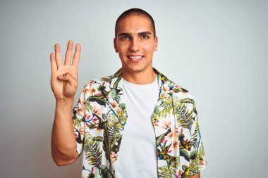 Tatilde, beyaz arka plan üzerinde Hawaii tişörtü giyen genç yakışıklı bir adam dört numaralı parmaklarıyla işaret ederken kendinden emin ve mutlu gülümsüyor..