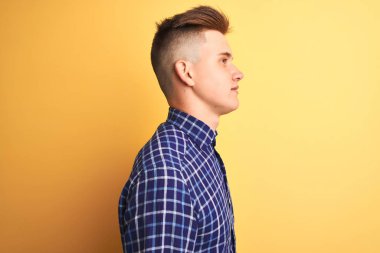 Sarı arka plan üzerinde duran, rahat bir görünüm veren, kendine güvenen bir gülümsemeye sahip genç ve yakışıklı bir adam..