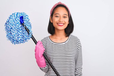 Genç Çinli temizlikçi kadın eldivenleriyle izole edilmiş beyaz arka planı paspaslıyor. Mutlu bir yüzü var ve gülümsüyor. Dişlerini gösteren bir gülümsemeyle.