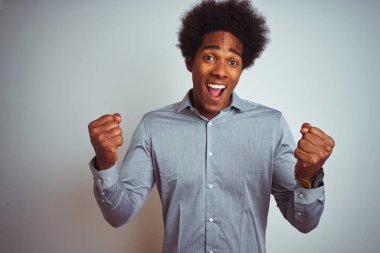 Afro saçlı, gri tişörtlü, izole edilmiş beyaz arka planı olan genç Afrikalı Amerikalı adam kollarını kaldırarak ve açık gözlerle başarının şaşkınlığını ve şaşkınlığını yaşıyor. Kazanan konsept.