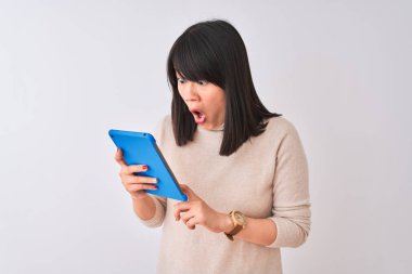 Güzel Çinli kadın mavi tablet kullanıyor. İzole edilmiş beyaz arka plan üzerinde duruyor. Şaşırmış bir yüz ifadesinden korkuyor ve heyecanlanıyor.