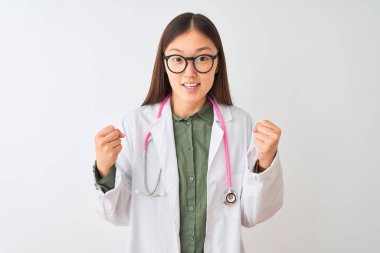 Genç Çinli kadın gözlüklü steteskop ile izole edilmiş beyaz arka plan üzerinde şaşırmış ve şaşırmış bir şekilde kollarını kaldırarak ve gözlerini açarak başarıyı kutluyor. Kazanan konsept.