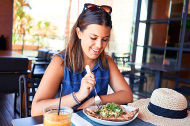 Genç ve güzel bir kadın restoranda oturmuş, yaz tatilinin tadını çıkarıyor ve lezzetli yemekler yiyor.