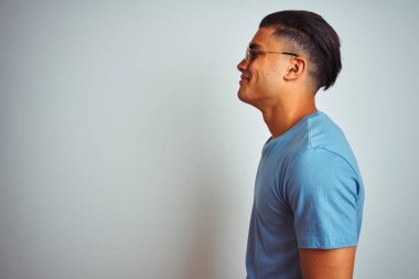 Mavi tişört ve güneş gözlüğü takan genç Brezilyalı adam beyaz arka planda, yan tarafa bakıyor, rahat poz veriyor, kendine güvenen bir gülümsemesi var..