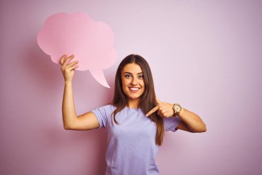 Genç, güzel bir kadın, pembe arka planda bulutlu konuşma balonu tutuyor. Sürpriz yüz ifadesiyle kendini gösteriyor.
