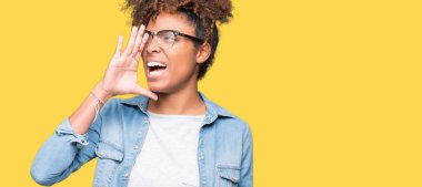 Bağırarak ve ağzı üzerinde el ile yan için çığlık izole arka plan üzerinde gözlük güzel genç Afro-Amerikan kadın. İletişim kavramı.