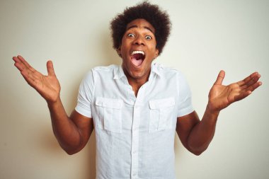 Afro saçlı Afrikalı bir adam, izole edilmiş beyaz arka planda dikilmiş çılgın ve başarısını kutluyor. Kolları havada ve gözleri açık, heyecanlı bir şekilde çığlık atıyor. Kazanan konsept