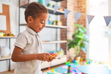 Güzel Afrikalı Amerikalı çocuk anaokulunda gülümseyen plastik çatal bıçakla oynuyor.
