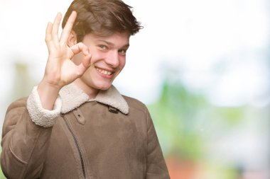 İzole arka plan el ve parmaklar ok işaretiyle yapıyor olumlu gülümseyen üzerinde kış ceket giyen genç yakışıklı adam. Başarılı ifade.