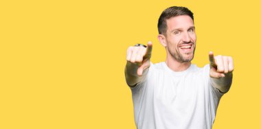 Olumlu ve neşeli gülümseyen casual beyaz t-shirt işaretleme ve parmaklar, kamerayla giyen yakışıklı adam