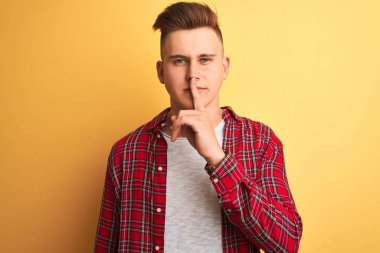 Sarı arka plan üzerinde duran ve dudakları dudaklarında sessiz olmak isteyen sıradan tişörtlü genç yakışıklı bir adam. Sessizlik ve gizli konsept.