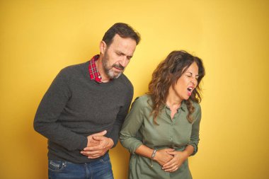 Güzel bir orta yaşlı çift, sarı arka planda, elleri midesinde, çünkü mide bulantısı, acı verici hastalıklar var. Ache kavramı.