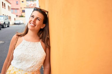 Turuncu duvara yaslanan güzel kız, güneşli bir yaz gününde gülümseyen genç arkadaş.