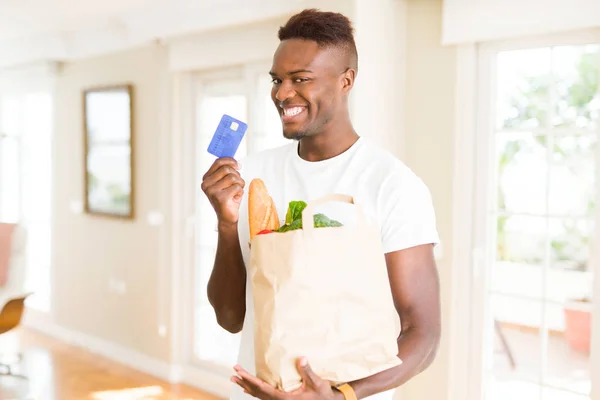 Hombre Afroamericano Sosteniendo Bolsa Papel Llena Comestibles Con Tarjeta Crédito —  Fotos de Stock