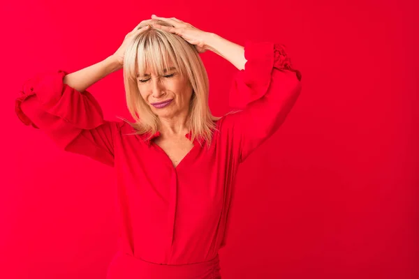 Middle age woman wearing elegant shirt standing over isolated red background suffering from headache desperate and stressed because pain and migraine. Hands on head.