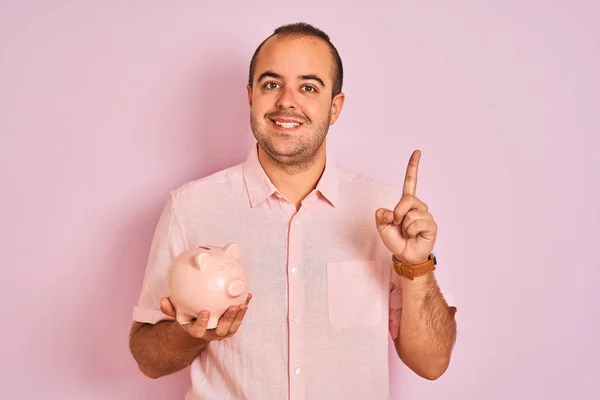 Joven Sosteniendo Piggybank Parado Sobre Fondo Rosa Aislado Sorprendido Con —  Fotos de Stock