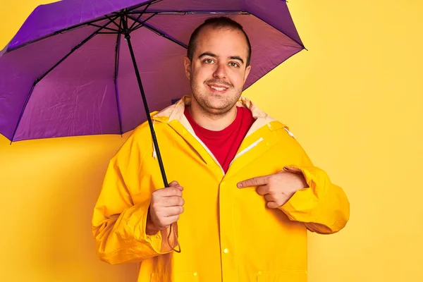 Mor Şemsiyeli Yağmurluk Giyen Genç Bir Adam Izole Edilmiş Sarı — Stok fotoğraf