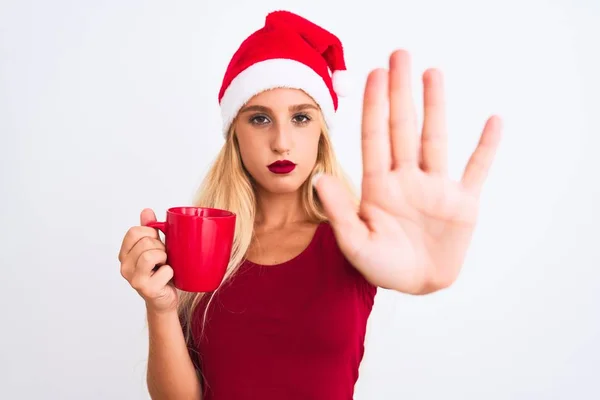 美しい女性を身に着けていますクリスマスサンタ帽子コーヒーを飲みます隔離された白い背景の上にオープンハンドでストップサインを行います深刻で自信を持って表現 防衛ジェスチャー — ストック写真