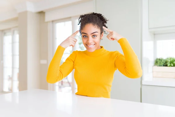 Beautiful african american woman with afro hair wearing a casual yellow sweater smiling pointing to head with both hands finger, great idea or thought, good memory