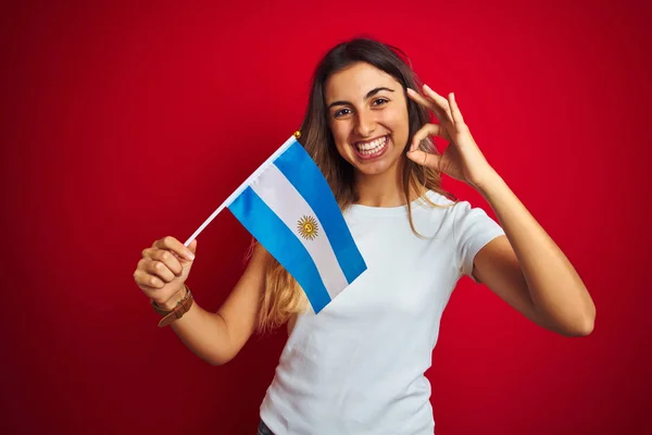 若いです美しいです女性保持Argentineフラグ上の赤隔離された背景を行いますOkサインとともに指 優れたシンボル — ストック写真