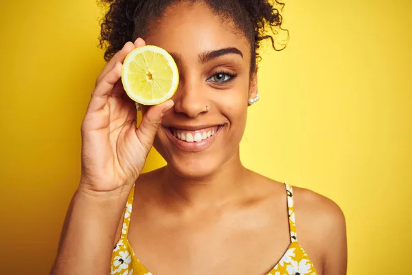 若いアフリカ系アメリカ人の女性がレモンのスライスを持っている孤立した黄色の背景の上に幸せな顔を立って笑顔歯を示す自信を持って笑顔で — ストック写真