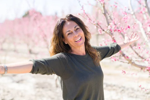 Beautiful middle age woman in the middle of pink peach flowers a