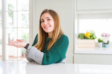 Güzel, iri yarı, sıradan çizgili bir süveter giyen genç bir kadın avuçları açık, fotokopi alanını gösteren, gülümseyerek mutlu bir gülümseme sunan,