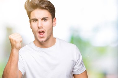 Öfkeli ve sinirli sinirli ve öfke ile bağırarak süre öfkeli yumruk yükselterek izole arka plan üzerinde beyaz t-shirt giyen genç yakışıklı adam. Öfke ve agresif kavramı.