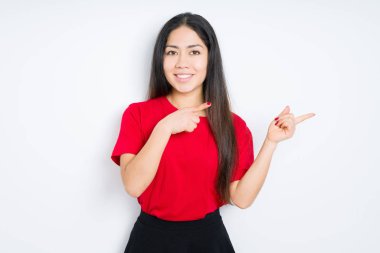 Güzel esmer kadın izole edilmiş arka planda kırmızı tişört giyiyor gülümsüyor ve kameraya bakıyor iki eliyle ve parmaklarıyla yüzünü gösteriyor..