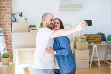 Yeni evde akıllı telefon kullanarak bir resim fotoğraf çekerken genç çift, yeni daireye taşımak için mutlu gülümseyen