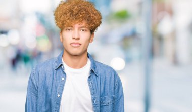 Yakışıklı genç afro saçlı kot ceket gevşek ciddi ifade ile yüzünde giyiyor. Basit ve doğal kameraya bakıyor.