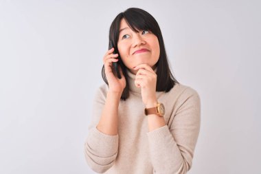 Akıllı telefondan konuşan genç, güzel bir Çinli kadın izole edilmiş beyaz arka planda ciddi bir yüz sorgulamayı düşünüyor, çok karışık bir fikir.