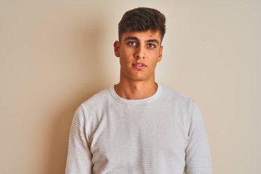 İzole edilmiş beyaz arka plan üzerinde duran kazak giyen genç Hintli adam yüzünde ciddi bir ifade var. Basit ve doğal bir şekilde kameraya bakıyorsun..