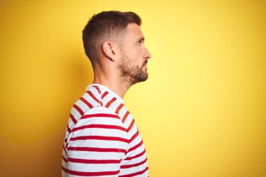 Sarı izole edilmiş arka plan üzerine gündelik kırmızı çizgili tişört giyen genç yakışıklı adam yan yana bakıyor, rahat poz veriyor kendine güvenen bir gülüşü var..