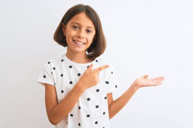 İzole edilmiş beyaz arka plan üzerinde duran gündelik tişört giyen genç ve güzel kız kameraya hayret ediyor ve gülümsüyor..