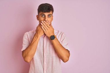 İzole edilmiş pembe arka planda duran günlük gömlekli genç Hintli adam yanlışlıkla ağızlarını kapatarak şok geçirdi. Gizli konsept.