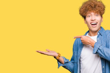 Afro saçlı denim ceket giyen genç yakışıklı adam şaşırttı ve el ile sunarken kameraya gülümseyerek ve parmak ile işaret.